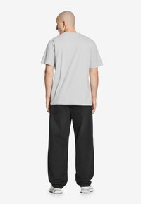 Szary t-shirt z krótkim rękawem i okrągłym dekoltem, w połączeniu z luźnymi czarnymi dżinsami. Stylizacja zawiera białe sneakersy, podkreślając casualowy charakter ubioru.