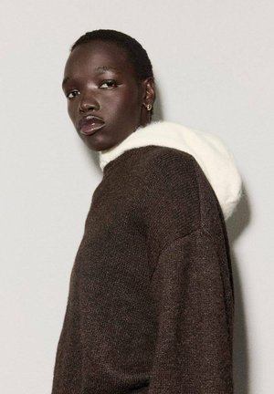 Suéter marrón con una suave capucha blanca, que presenta un patrón tejido texturizado. El rostro del modelo está girado levemente, mostrando un acabado suave y brillante en los labios.