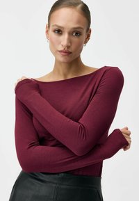 Bordowa bluzka z długim rękawem, szerokim dekoltem i dopasowanym krojem. Miękki, elastyczny materiał z otworami na kciuki w rękawach.