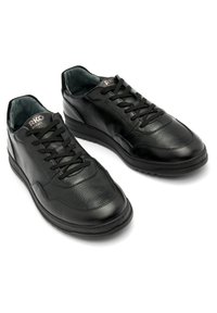 Černé kožené tenisky mají texturovaný povrch, kulatou špičku, šněrovací design a polstrovaný límec s nenápadným logem na jazyku.