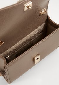 Ruskean kuvioidun nahkalaukun sisäpuoli, jossa on vetoketjullinen tasku ja korttipaikat, kullanväriset yksityiskohdat ja magneettinen napsalukko.