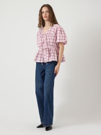 Blusa a quadri rosa e bianca con maniche a sbuffo e fiocchi frontali, abbinata a jeans a gamba dritta blu scuro a vita alta e scarpe nere con punta a cono.