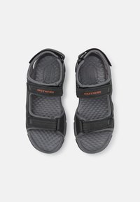 Svarta sandaler med texturerade gummisulor, justerbara Velcro-remmar och "Skechers"-logotyp i orange. Dämpning för komfort och stöd.