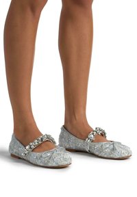 Bailarinas de tela azul claro con diseño texturizado, adornadas con cristales en la correa y lazo en la punta, suela plana.