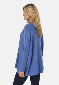 Suéter azul de punto con un corte relajado, mangas largas, textura acanalada en los puños y un cuerpo liso, combinado con jeans oscuros.