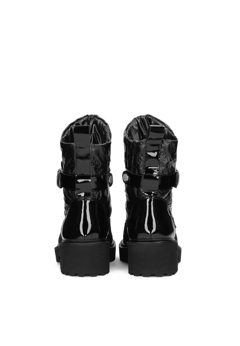 Un paio di stivaletti neri in pelle verniciata con suole spesse, tomaia in tessuto trapuntato e cinturini decorativi visti da dietro.