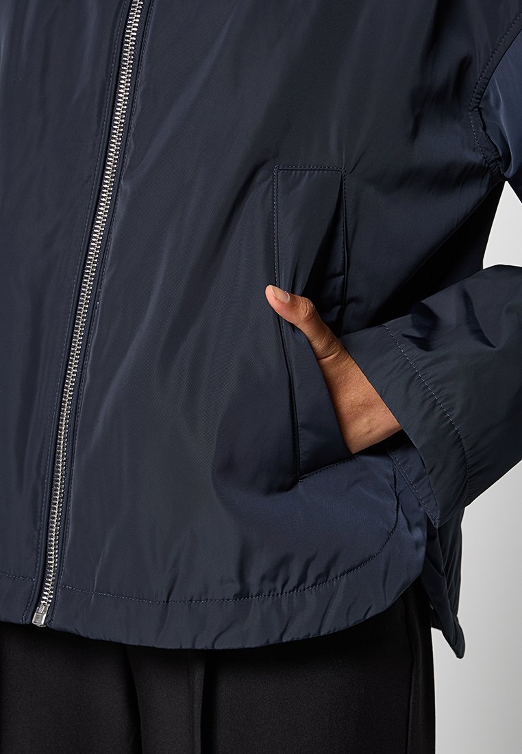 Marineblauwe, lichtgewicht jas met een ritsluiting, zijzak en elastische boorden. Soepele textuur met een waterafstotende afwerking.