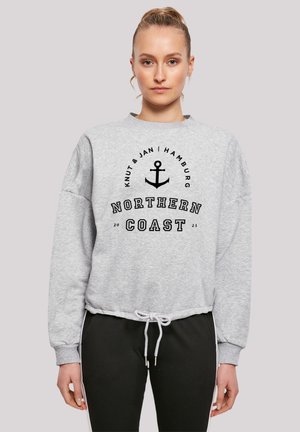 Helle graue Sweatshirt mit geripptem Ausschnitt und weiten Ärmeln, das ein schwarzes Anker-Graphic und den Text "NORTHERN COAST" in fetter Schrift trägt.
