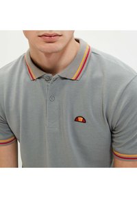 Graues Poloshirt mit einer Zwei-Knopf-Leiste, geripptem Kragen mit roten und gelben Streifen und einem gestickten Logo auf der linken Brust.