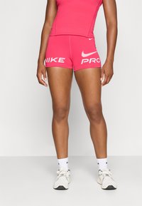 Ružové šortky Nike Pro s bielym logom, s priliehavým strihom a mäkkým materiálom. Spárované s bielymi športovými topánkami a ponožkami.