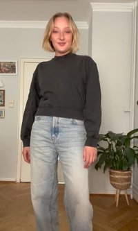 Sweatshirt preto cropped com decote redondo, combinado com jeans de perna reta azul claro. Tecido suave, ajuste casual, design minimalista.