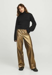 Maglione nero a collo alto in maglia con maniche lunghe abbinato a pantaloni a gamba larga in metallo dorato a vita alta. Scarpe con plateau nere e spesse.