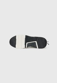 Svart og hvit såle til sneakers med teksturert gummioverflate, spor for grep, og en hvit mellomsåle med et distinkt utskjæringsdesign.