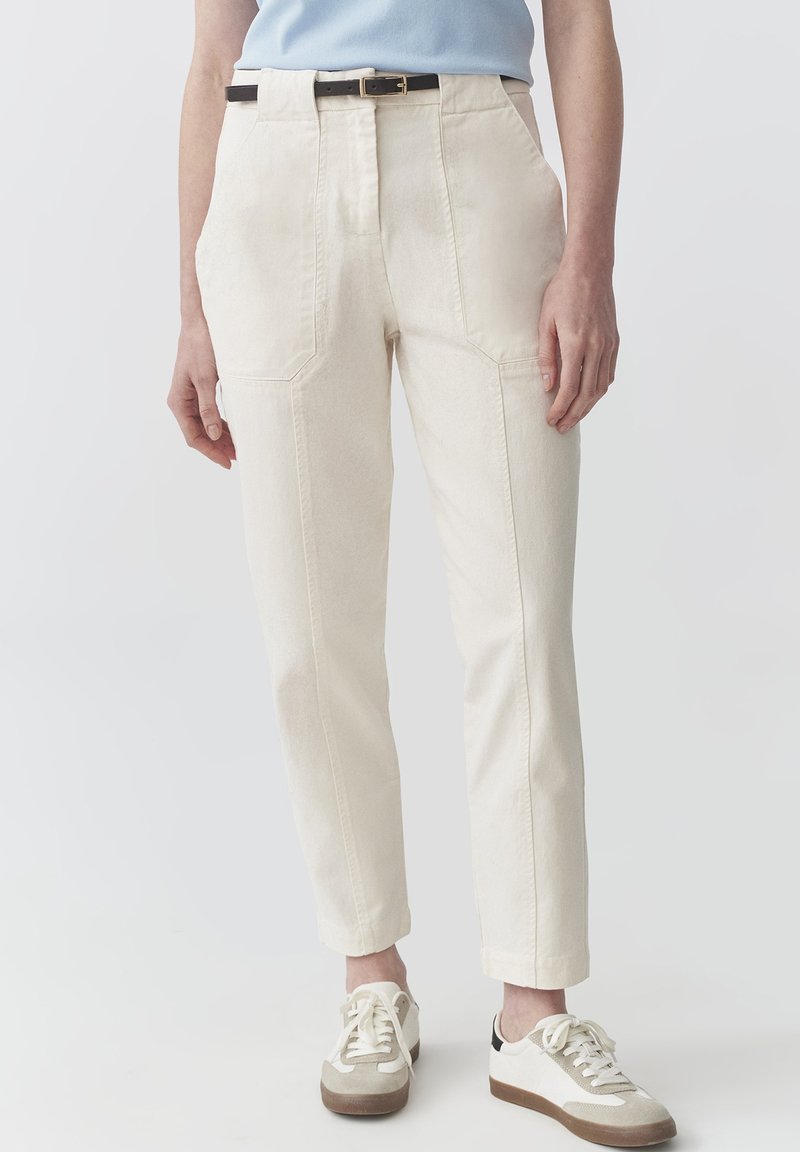 Pantalones de tiro alto color crema, con bolsillos laterales y costuras visibles. Combinados con zapatillas blancas y beige.