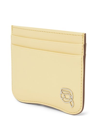Porte-cartes en cuir fin jaune pâle avec trois emplacements pour cartes et un petit logo métallique représentant un visage portant des lunettes et un bandeau.