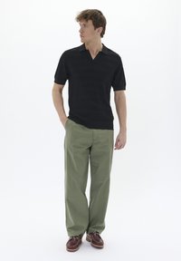 Črna kratka polo majica z V-izrezom, v kombinaciji z svetlo zelenimi širokimi hlačami in rjavimi čolnarskimi čevlji. Preprosta, teksturirana pletenina.