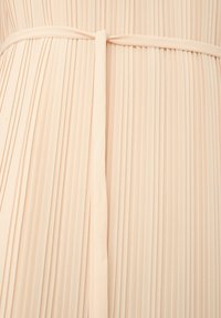 Tissu plissé beige avec une fine ceinture nouée autour de la taille, créant des plis verticaux espacés de manière régulière et une texture lisse.