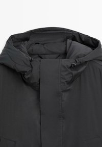 Sort polstret jakke med høj krave, der har snorejustering og glat tekstur. Minimalistisk design uden synlige mønstre.