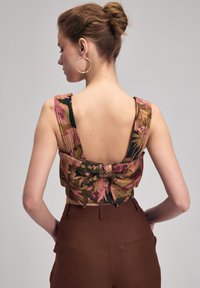 Blomstret cropped top med brede stropper og lav rygdesign. Farverne inkluderer pink, grøn og brun. Stylet med højtaljede brune bukser.