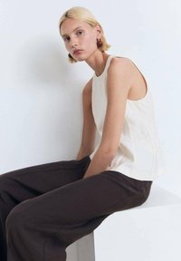Cream sleeveless top with a straight cut, paired with loose brown trousers. Smooth fabric with subtle seams and minimalistic design details.