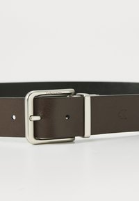 Brown leather belt with a polished silver rectangular buckle. Features discrete logo engraving, multiple holes for adjustment, smooth texture.