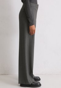 Sive široke hlače napravljene od teksturirane tkanine, s bočnim džepovima i jednostavnim dizajnom. Uparene s crnim debelim cipelama.