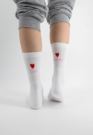 Weiße gerippte Socken mit einem roten Herz und pinkem Text "CIAO" auf einer Socke und "AMORE" auf der anderen, mit glatter Textur.