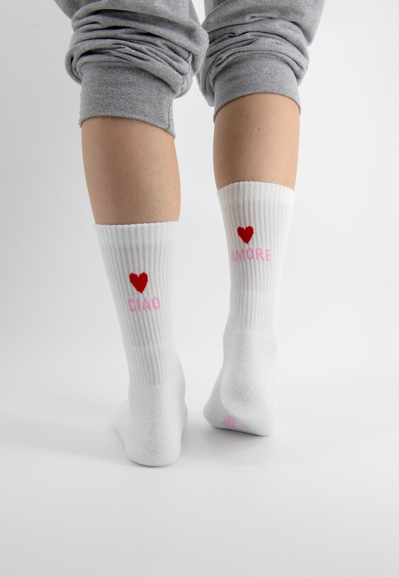 Weiße gerippte Socken mit einem roten Herz und pinkem Text "CIAO" auf einer Socke und "AMORE" auf der anderen, mit glatter Textur.
