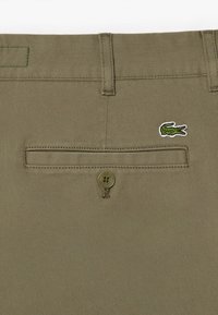 Licht olijfgroen katoenen broek met een achterzak, voorzien van een ronde knoop en geborduurd krokodillologo. Getextureerde twill stof.