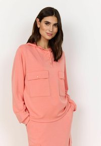 Perzikkleurige hoodie met lange mouwen, knopenlijst en twee voorzakken. Zachte stof met een relaxed fit. Gladde textuur, minimalistisch ontwerp.