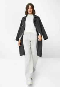 Mørkegrå uldfrakke med brede klapper, over en hvid turtleneck. Lysegrå bukser med bred ben og hvide sneakers fuldender outfittet.