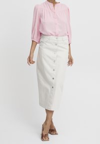Blusa rosa chiaro con punti testurizzati, tessuto semi-trasparente e chiusura a bottoni. Gonna di jeans color crema, a lunghezza ginocchio, con bottoni frontali.
