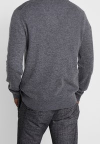 Grijze wollen trui met een ronde halslijn en geribde mouwen, gecombineerd met gestreepte grijze broek. Gelaagd stof, aansluitend ontwerp.