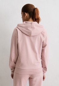 Jasnoróżowa bluza z kapturem o miękkiej fakturze, z kapturem na sznurki i ściągaczami na rękawach, zaprojektowana z myślą o luźnym kroju.