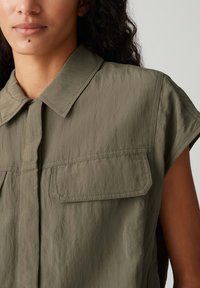 Olijfgroene utility shirt met korte mouwen, een knoopsluiting aan de voorkant, twee borstzakken en een gestructureerde stof. Heeft zichtbare stiksels.