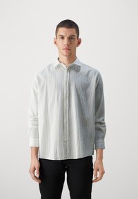 Lichtgrijs lange mouwen shirt met een gestructureerde afwerking, knoopsluiting aan de voorkant en een klassieke kraag. Draagt met zwarte broek voor contrast.