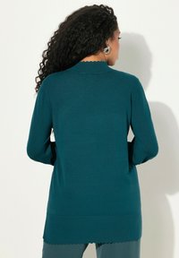 Tiefblau gestrickter langärmeliger Pullover mit einem gewellten Rundhalsausschnitt und Saum, der eine glatte Textur und eine figurbetonte Passform aufweist, von hinten gezeigt.
