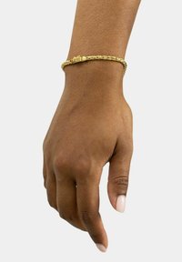 Bracciale intrecciato in oro su una mano, con chiusura a cerniera e trama intricata, su uno sfondo semplice.