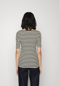 Mustat ja valkoiset raidalliset lyhythiaiset paita, jossa on pyöreä pääntie ja teksturoitu ribbikangas, yhdistettynä tummansinisiin farkkuihin.