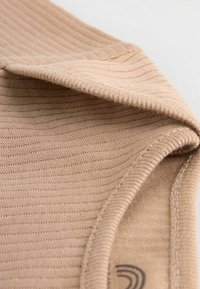 Beige Rippstoff mit einer weichen Textur, ausgestattet mit einem gerollten Kragen und feinen Nähdetails in der Nahansicht.