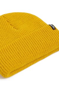 Beanie giallo lavorato a maglia con un design texturizzato a coste. Presenta un risvolto e una piccola etichetta nera sul lato.