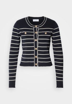Granatowy kardigan z białymi poziomymi paskami, złotymi guzikami i falbaniastym dołem. Posiada dwie przednie kieszenie i okrągły dekolt.