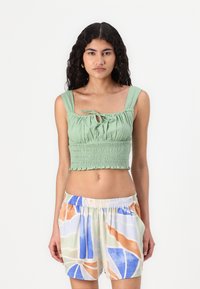 Haut cropped vert avec un design smocké et un lien ajustable au centre. Associé à un short ample multicolore avec des motifs abstraits.