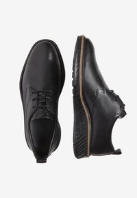 Scarpe in pelle nera con una finitura liscia, caratterizzate da un design con lacci, punta arrotondata e una suola marrone a contrasto.
