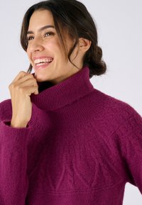 Jersey de punto color fucsia con cuello alto de canalé, patrón texturizado y mangas anchas, confeccionado con tela suave.