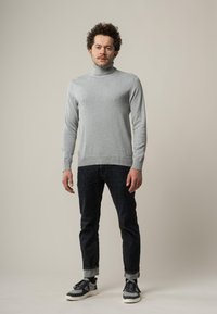 Hellgrauer Rollkragenpullover aus Strickstoff, kombiniert mit dunkelblauen Jeans und lässigen Sneakers mit einer weißen Sohle und marineblauen Akzenten.