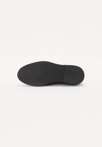 Black sole of a shoe with a smooth, textured surface. Rounded toe design and slight indentation near the heel. No visible patterns or accents.