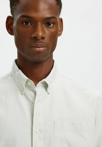 Πουκάμισο με κουμπιά σε ανοιχτό πράσινο χρώμα με λεπτές λευκές ρίγες. Διαθέτει κλασικό γιακά και τσέπη στο στήθος. Μαλακό ύφασμα με λεία υφή.