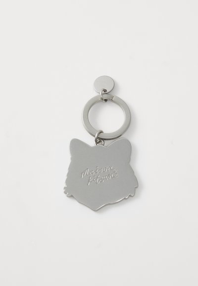 Porte-clés en argent en forme de tête de chat avec texte gravé "Maison Kitsuné" et un anneau de fixation circulaire. Texture lisse et brillante.