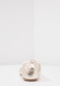 Metalen gouden platte schoen met een zachte stoffen rand aan de achterkant en een afgeronde vorm. Gladde textuur en minimalistisch ontwerp.